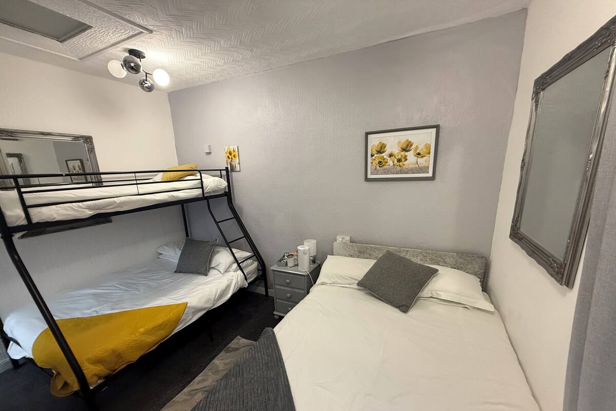 Ein Schlafraum mit Etagenbetten, einem Schreibtisch, einem gerahmten Bild an der Wand und einer Deckenleuchte.