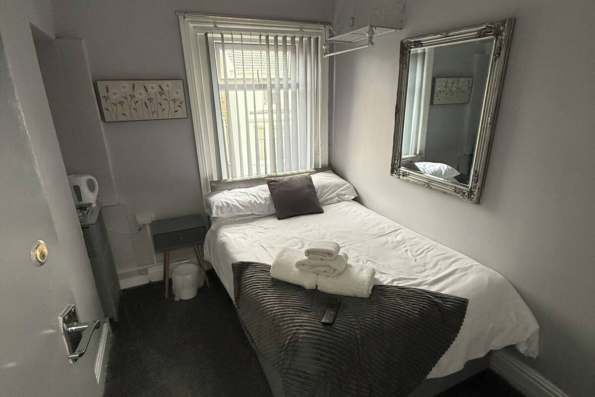 Ein Schlafzimmer mit einem Bett, einem Nachttisch, einem Spiegel, einem Fenster mit Jalousien und einer Tür.