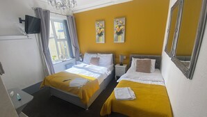 Una habitación de hotel con dos camas, un televisor, una ventana con cortinas y una obra de arte en la pared.