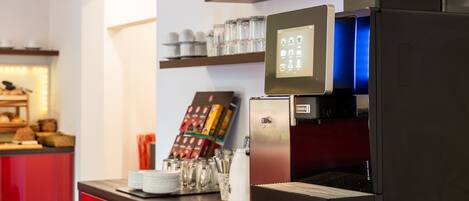 Una máquina de café con pantalla digital, una estación de café con tazas y un menú, y un estante con cristalería.
