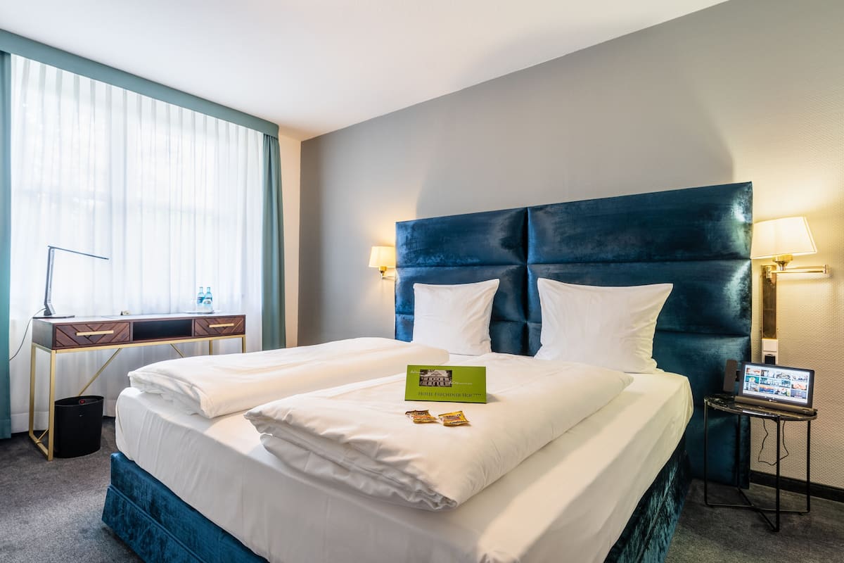 A hotel room with a large bed, a desk with a lamp, and a laptop on a side table.