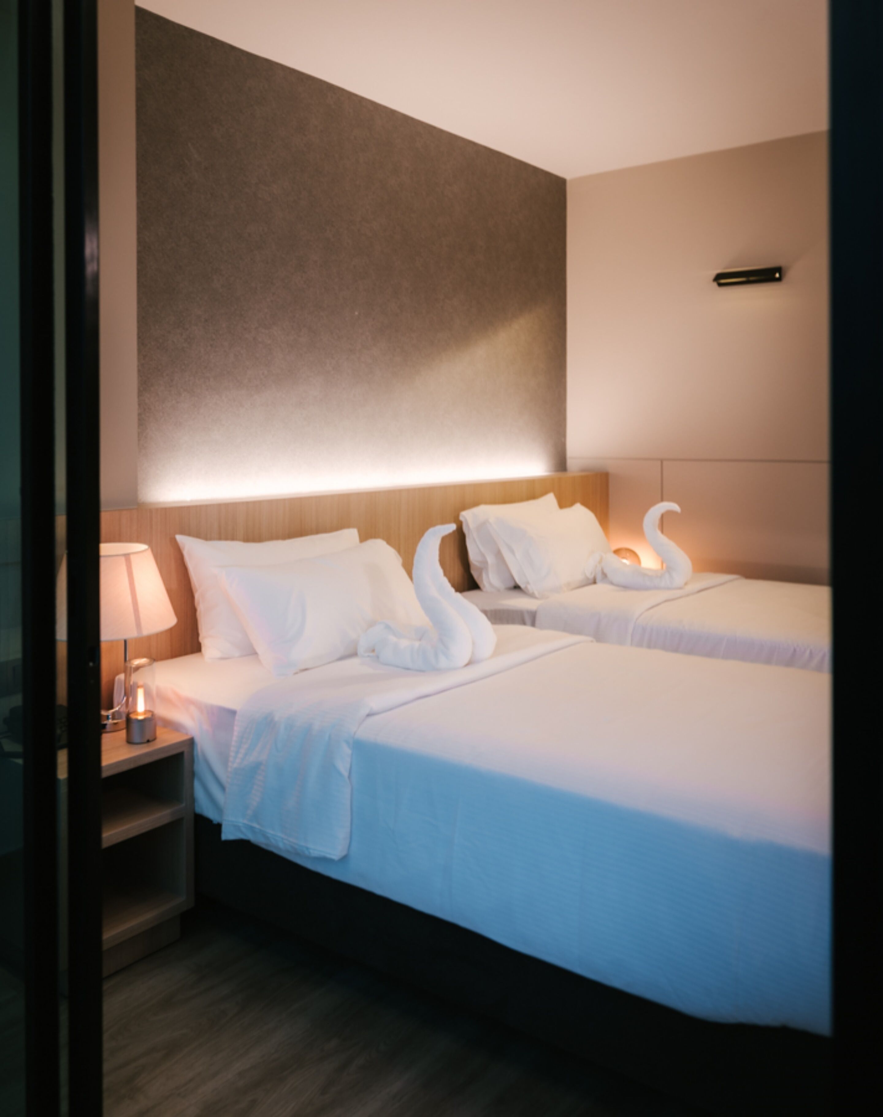 Een hotelkamer met twee bedden, een nachtkastje, een lamp en een wandairconditioner.
