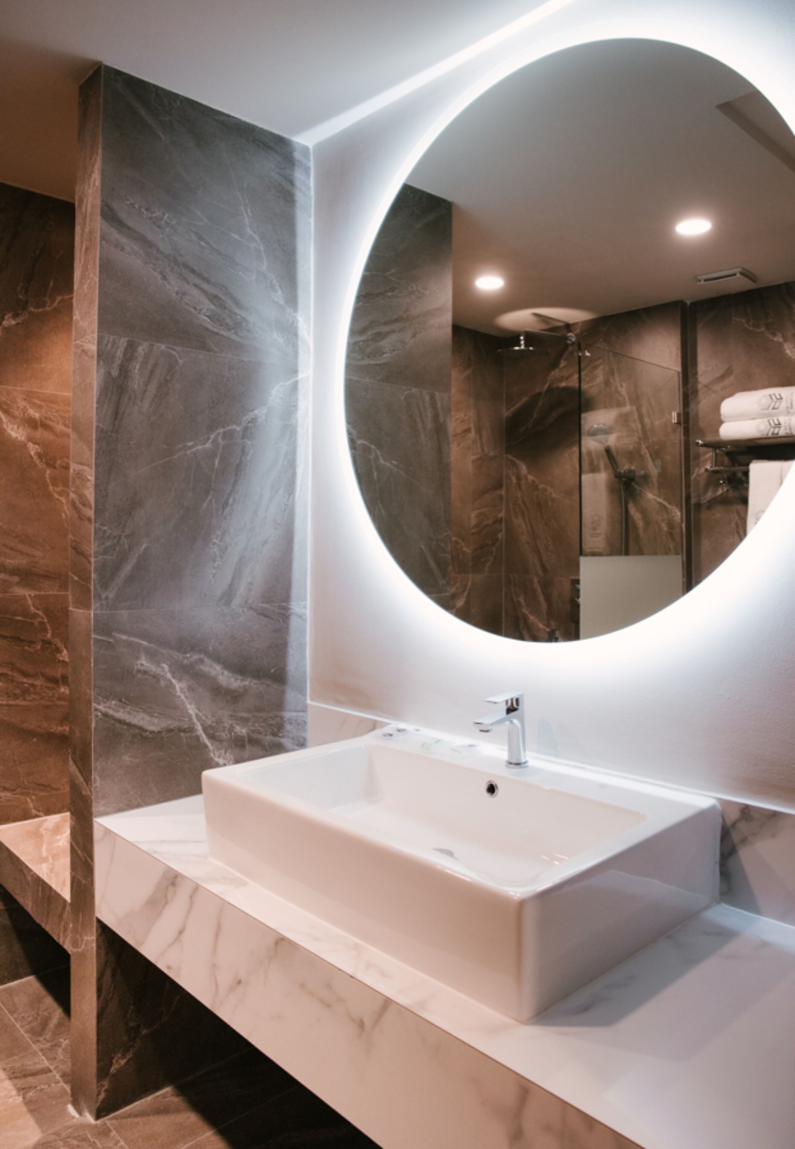 A modern bathroom with a marble vanity, a large mirror, and a shower area.