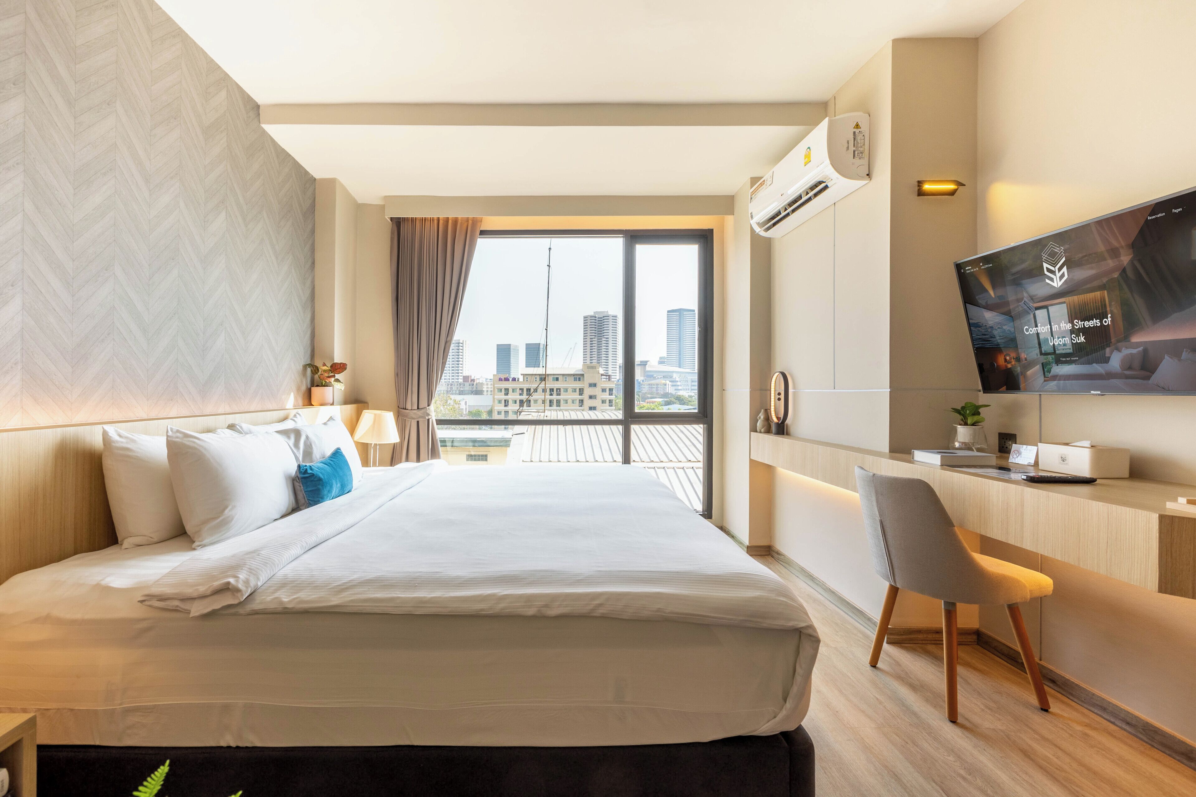 A modern hotel room with a large bed, a desk with a chair, a TV, and a city view.