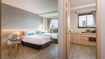 A hotel room with two beds, a desk, a window with a city view, and a herringbone-patterned wall.