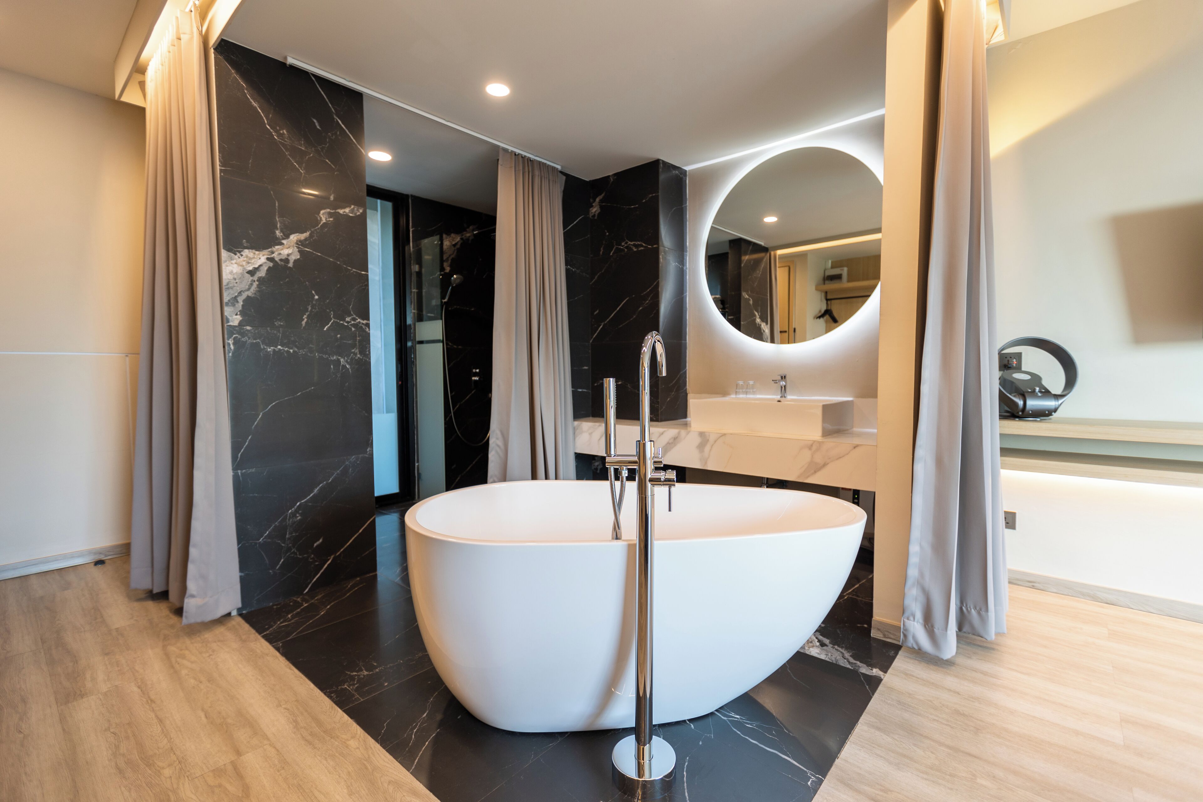 Ein modernes Badezimmer mit freistehender Badewanne, Marmorwänden und einem großen Spiegel.