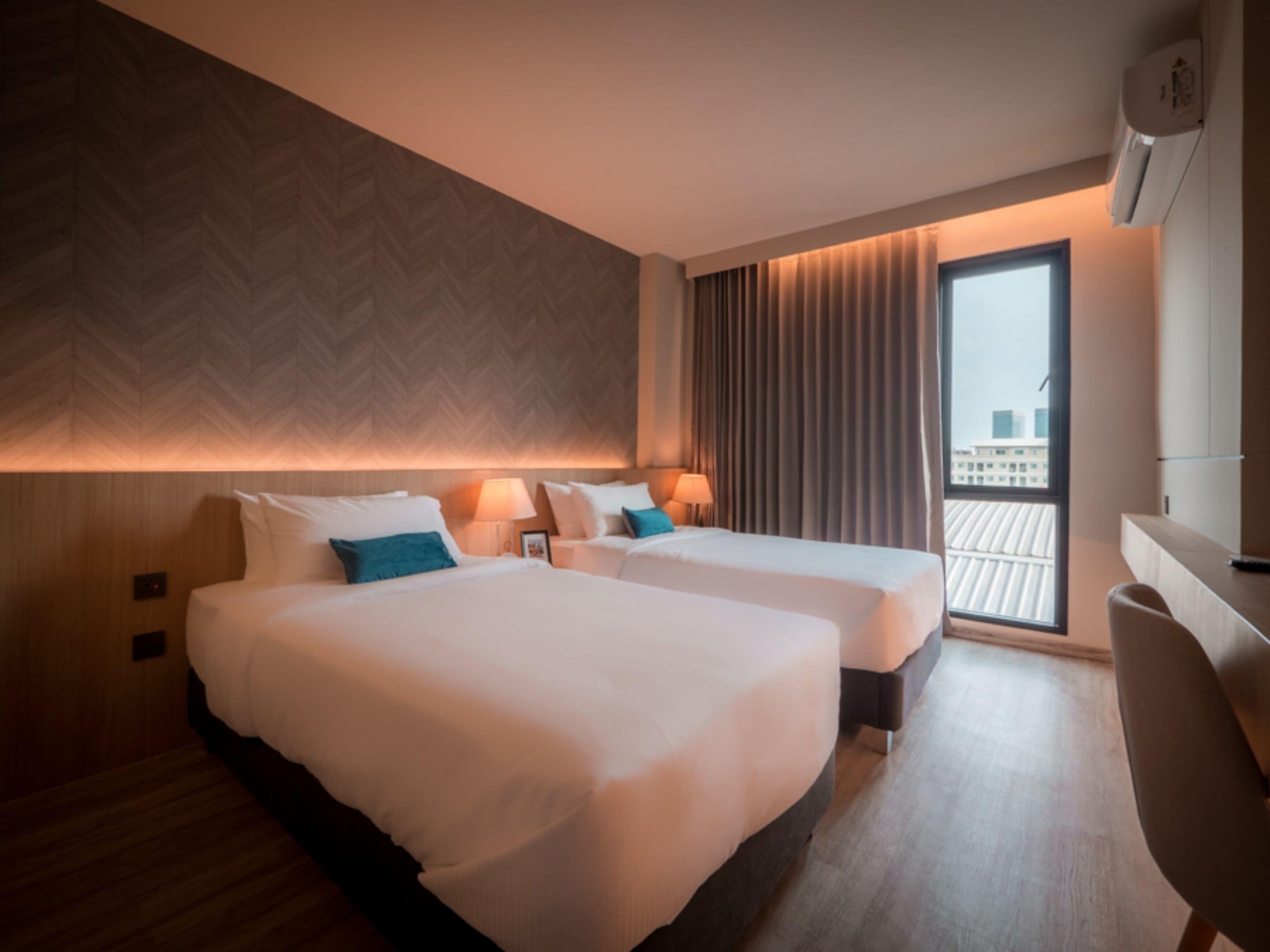 A hotel room with two beds, a desk, and a large window with a view of the city.