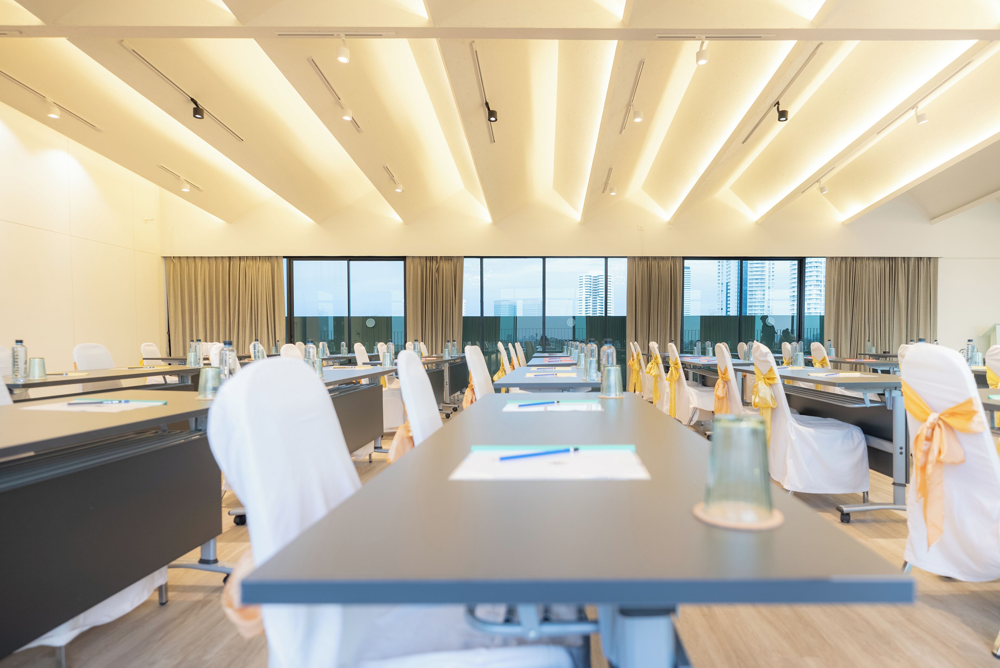 A conference room with a long table, chairs with yellow sashes, and large windows with a city view.