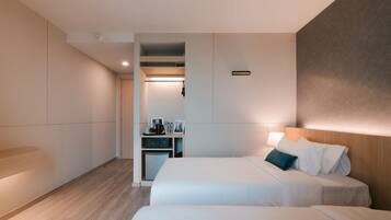 A modern hotel room with two beds, a desk, and a walk-in closet.