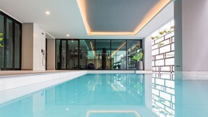 Una piscina interior moderna con agua cristalina, paredes de vidrio e iluminación empotrada en el techo.