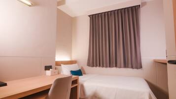 Una habitación de hotel con cama, escritorio, silla, mesita de noche y ventana con cortinas.