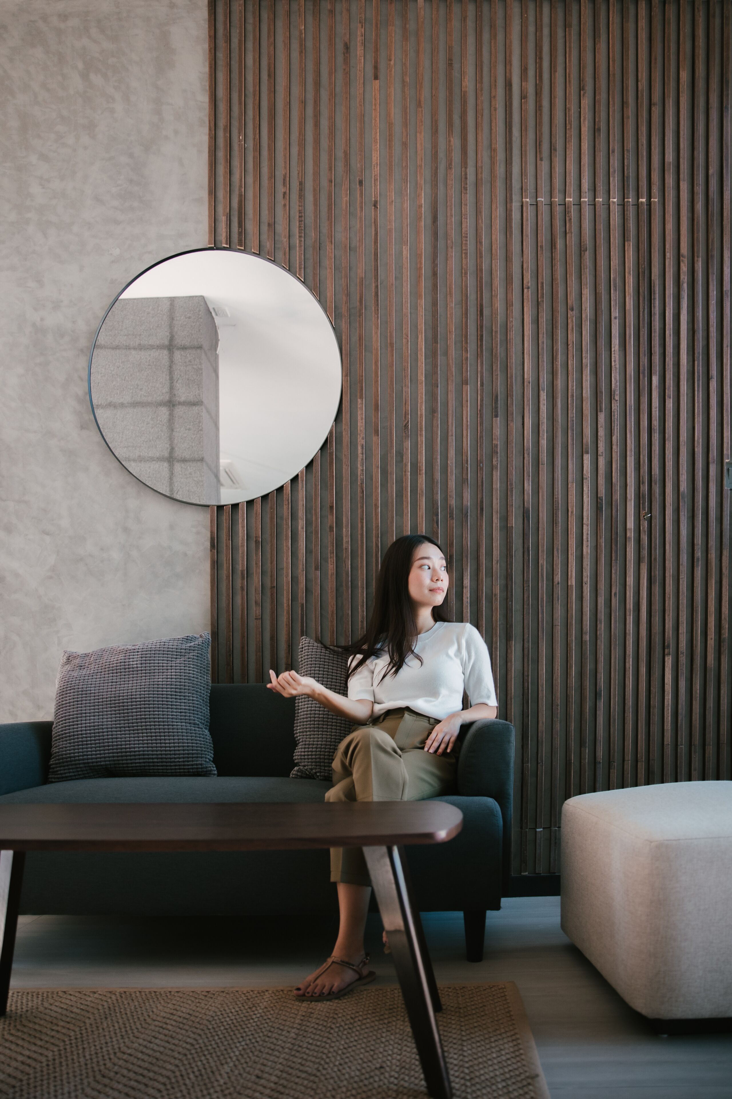 A modern living room with a sofa, a round mirror, and a wooden slat wall.