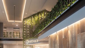 Un lobby moderno de hotel con un mostrador de recepción, un sofá con cojines, una escalera con plantas y un letrero que dice "Fifty-Six".