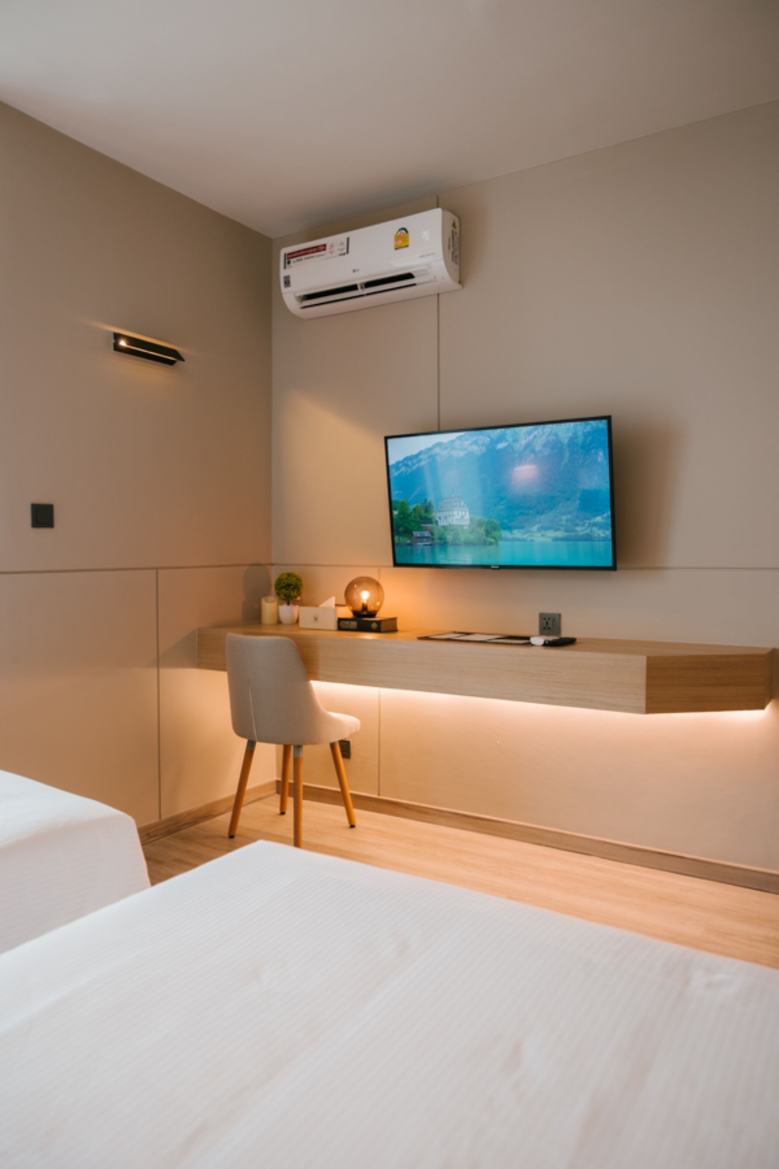 Una moderna camera d'albergo con televisione a schermo piatto montata a parete, una scrivania in legno con una sedia e un letto con biancheria da letto bianca.