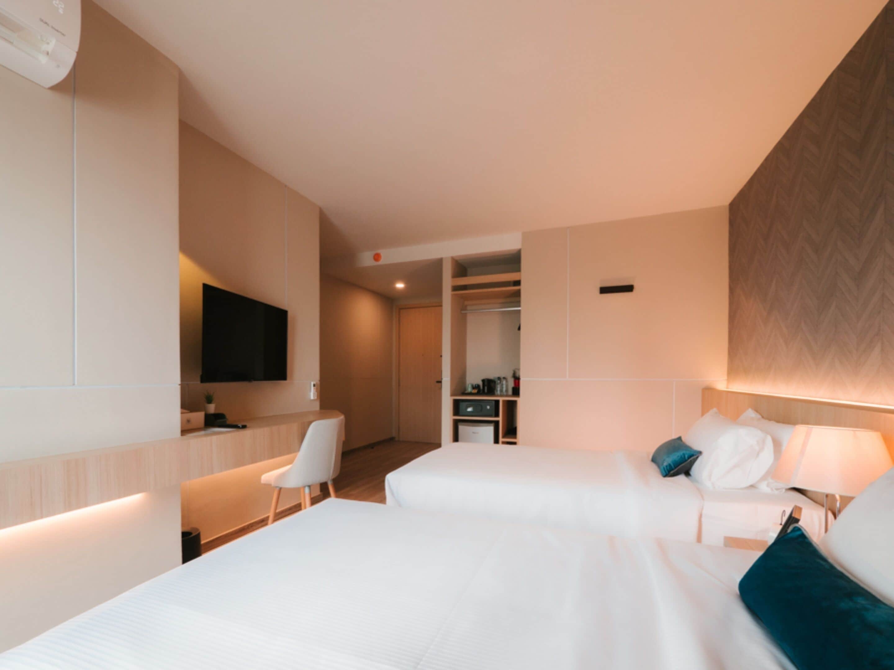 A hotel room with two beds, a desk, a chair, a TV, and a closet.