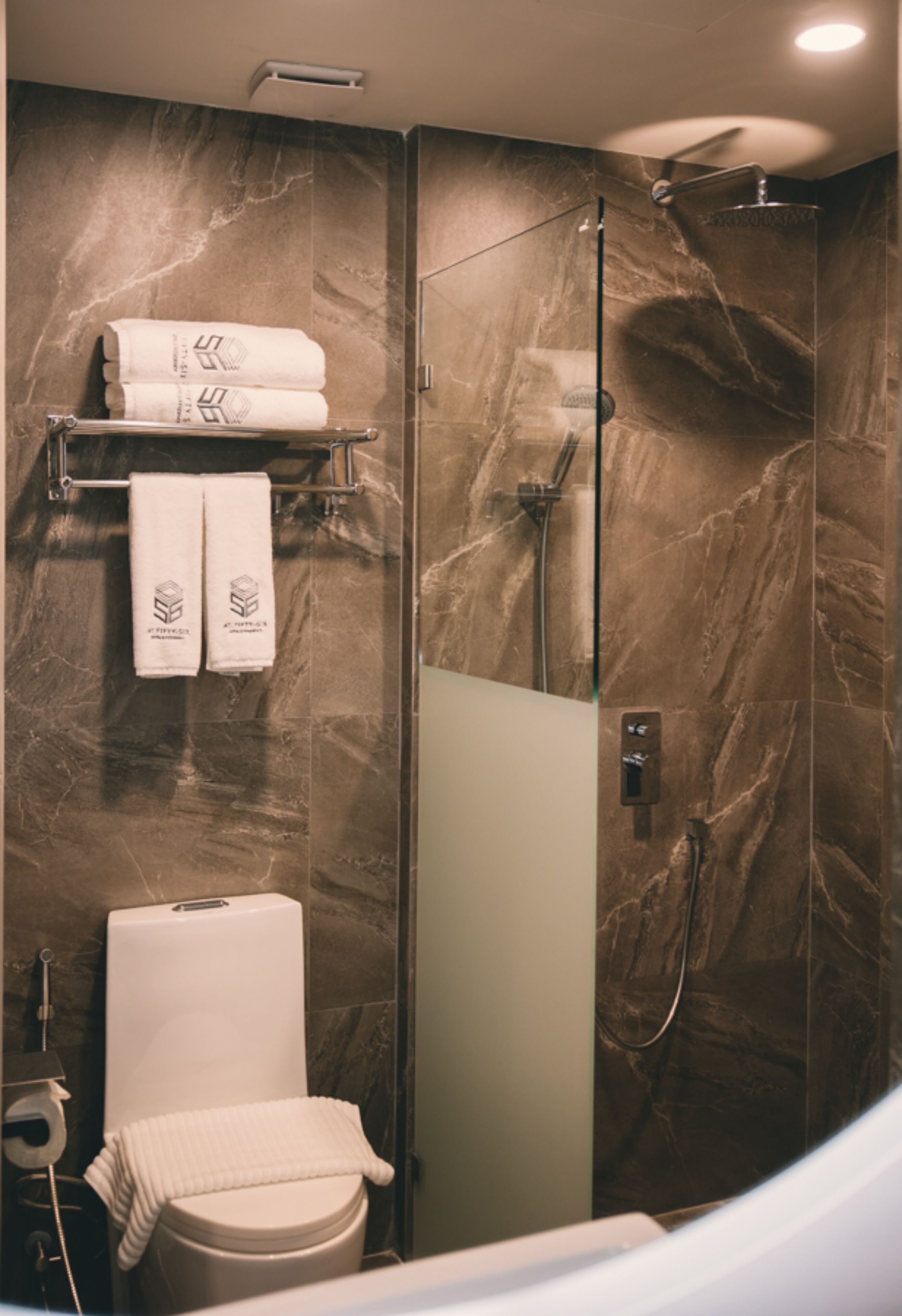 A bathroom with a marble wall, a toilet, a shower, and a towel rack with two towels.
