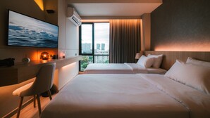 Habitación de hotel con cama, escritorio, silla, ventana grande con cortinas y vista a la ciudad.