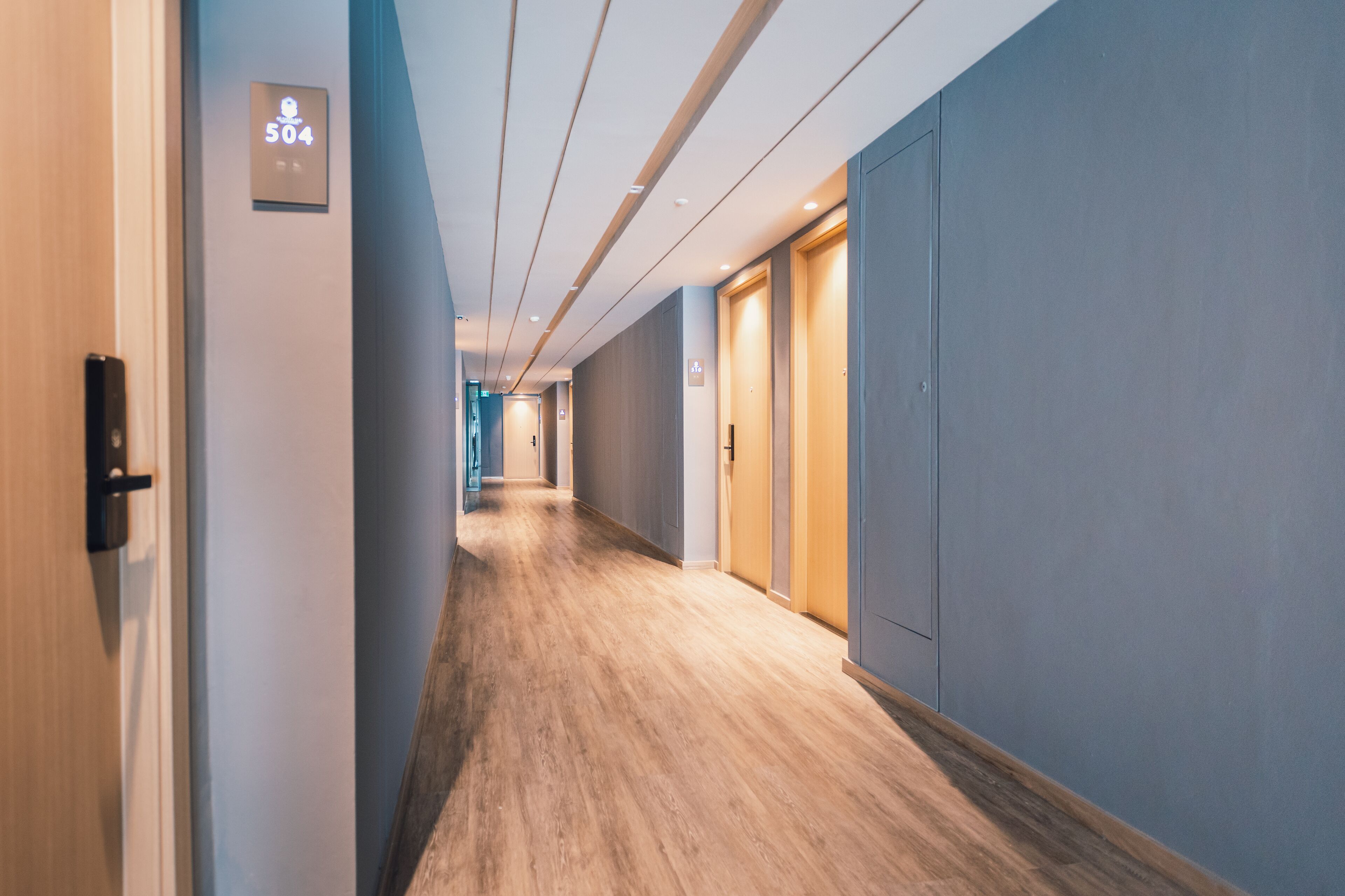 A hotel hallway with a wooden floor, blue walls, and doors on the right.