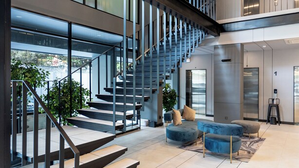 Un interior moderno con una escalera, zona de estar y grandes ventanales.