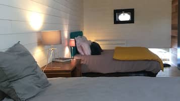 A bedroom with a wooden ceiling, a bed with a gray blanket, a bedside table with a lamp, and a framed picture on the wall.