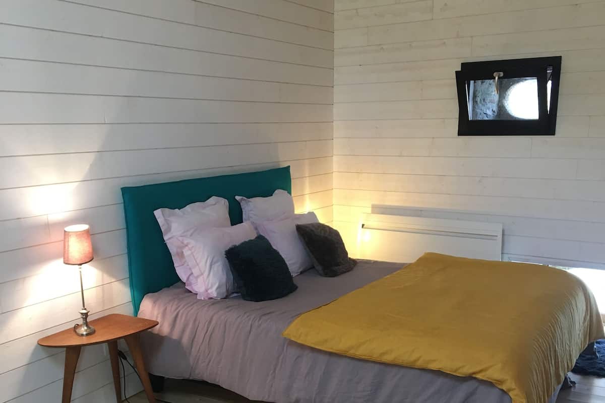 A bedroom with a bed, pillows, a bedside lamp, a rug, and a window.