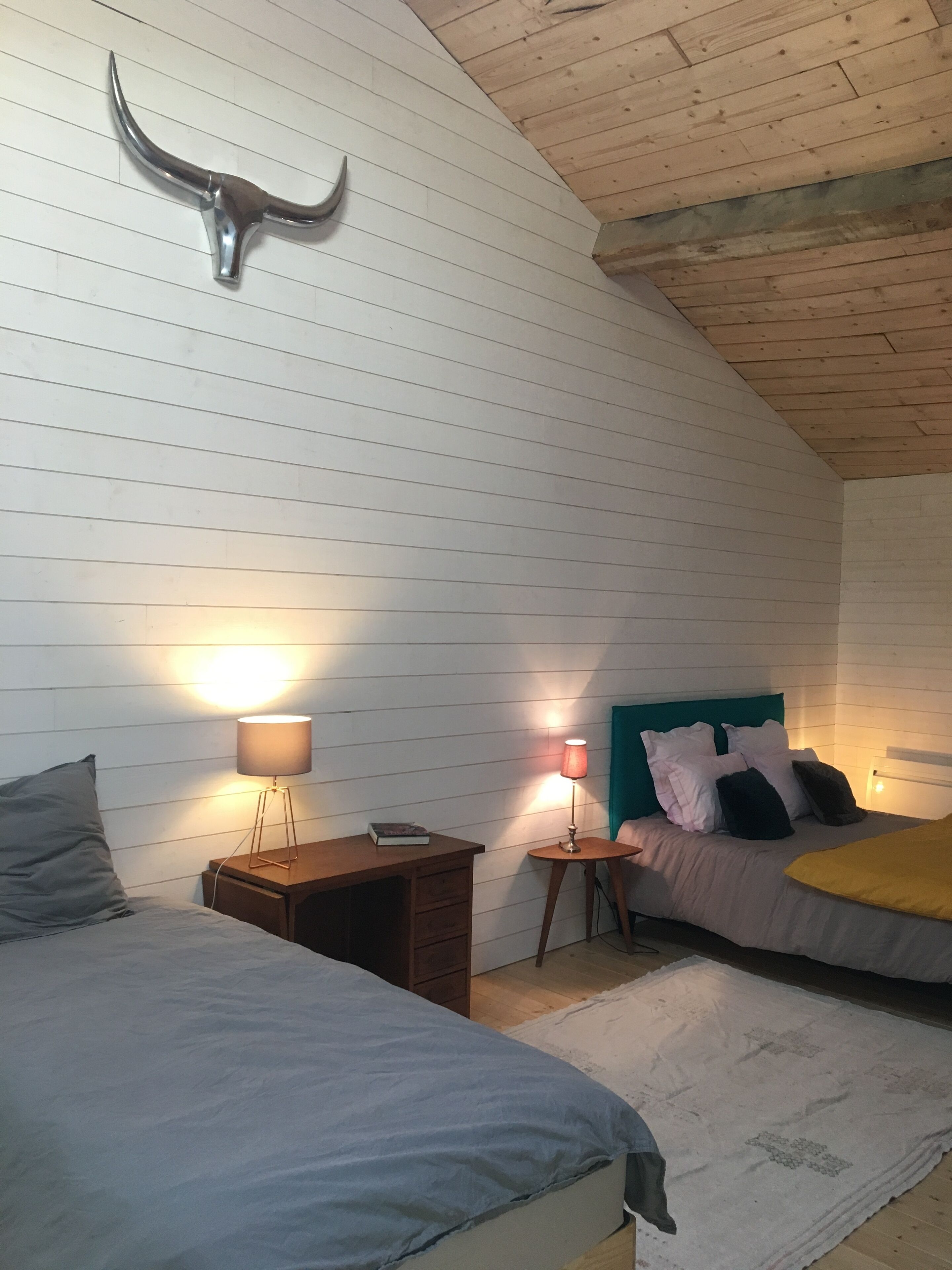 A bedroom with two beds, a wooden ceiling, and a bull's head decoration on the wall.