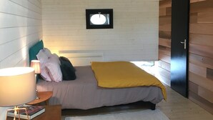 Un dormitorio con cama, mesita de noche, lámpara, un cuadro enmarcado en la pared y una puerta de madera.