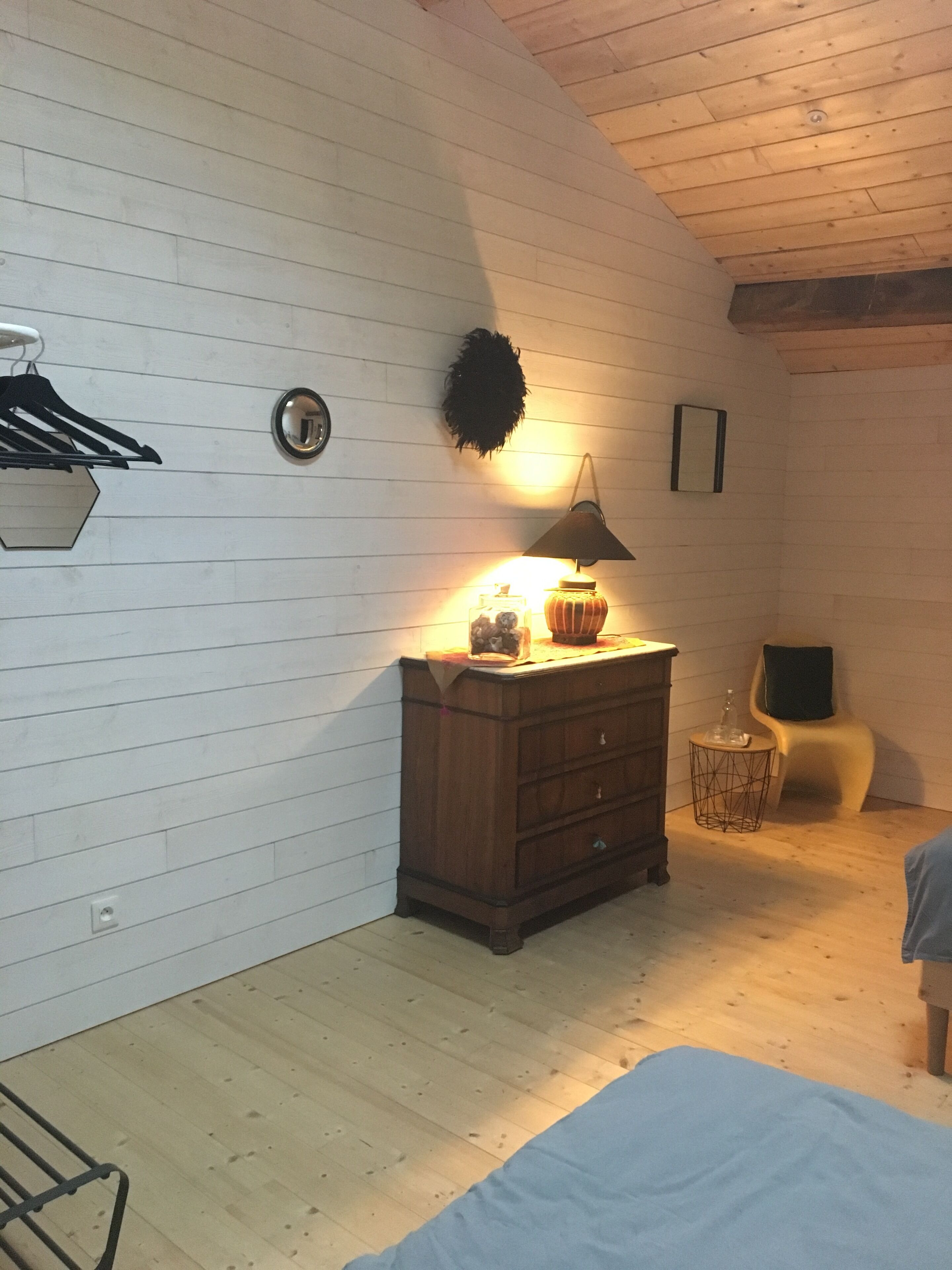 Una habitación con un aparador de madera, una lámpara, una silla y una cama.