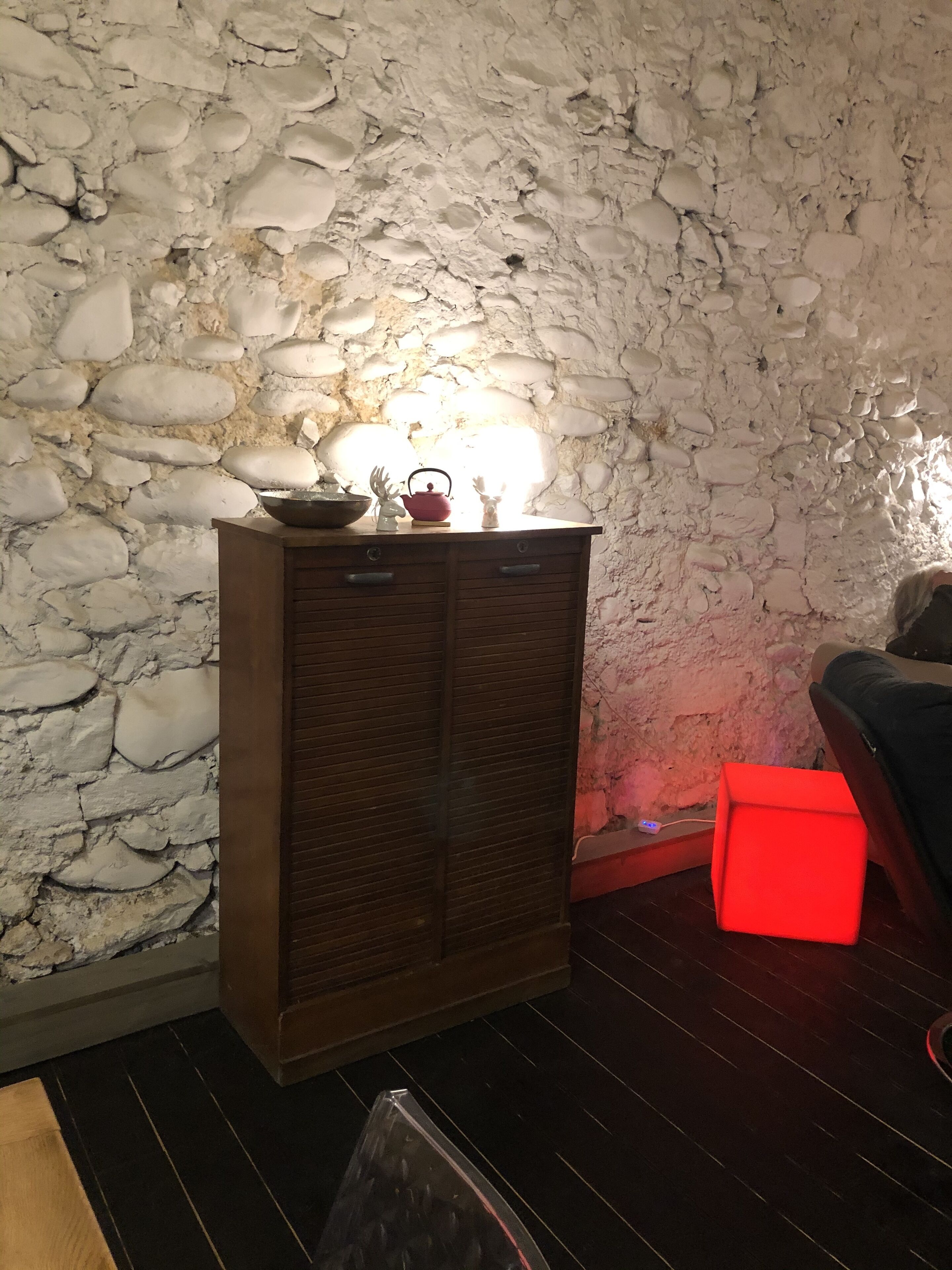 Une pièce avec un mur en pierre, un meuble en bois, une boîte rouge et un canapé.