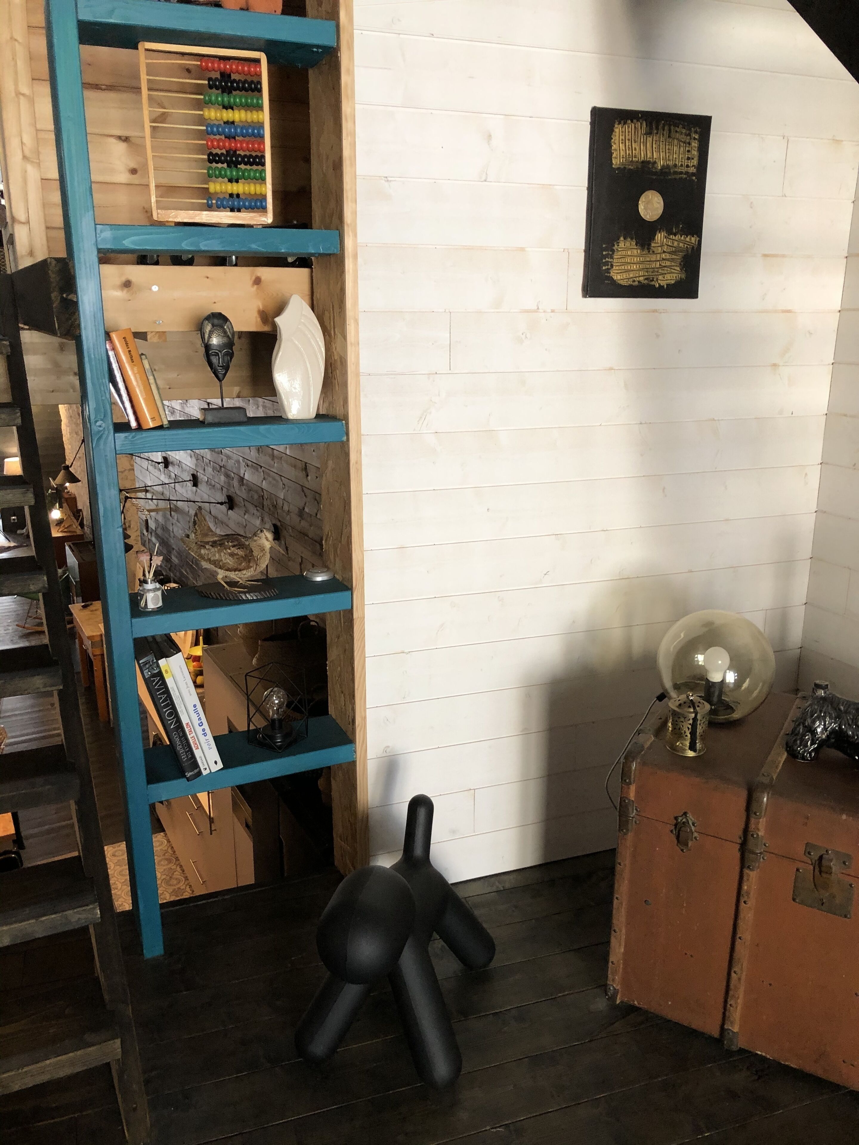 A room with a wooden bookshelf, a small statue, a globe, and a suitcase.
