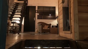 Un interior de madera con una escalera que conduce a un segundo piso, una silla de mimbre y una pequeña mesa con una vela.