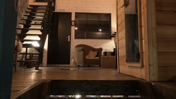 Un interior de madera con una escalera que conduce a un segundo piso, una silla de mimbre y una pequeña mesa con una vela.