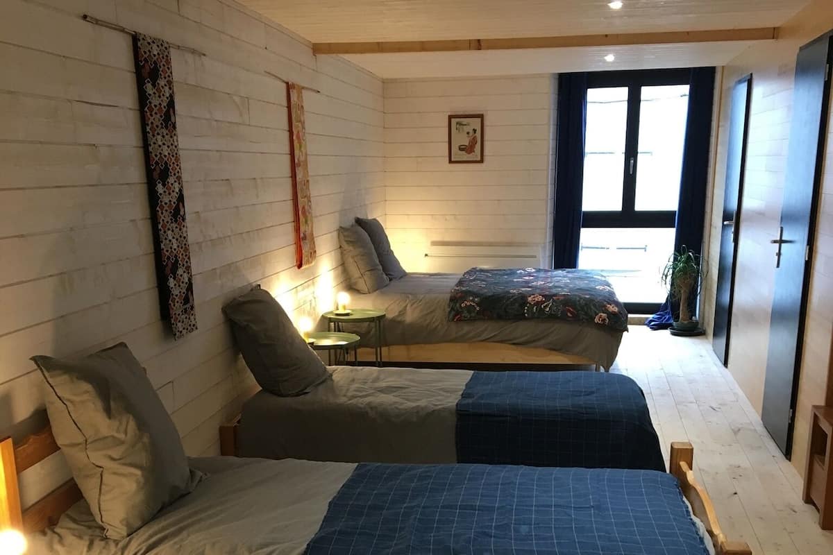 A cozy room with two beds, a small table with a lamp, and a window with curtains.