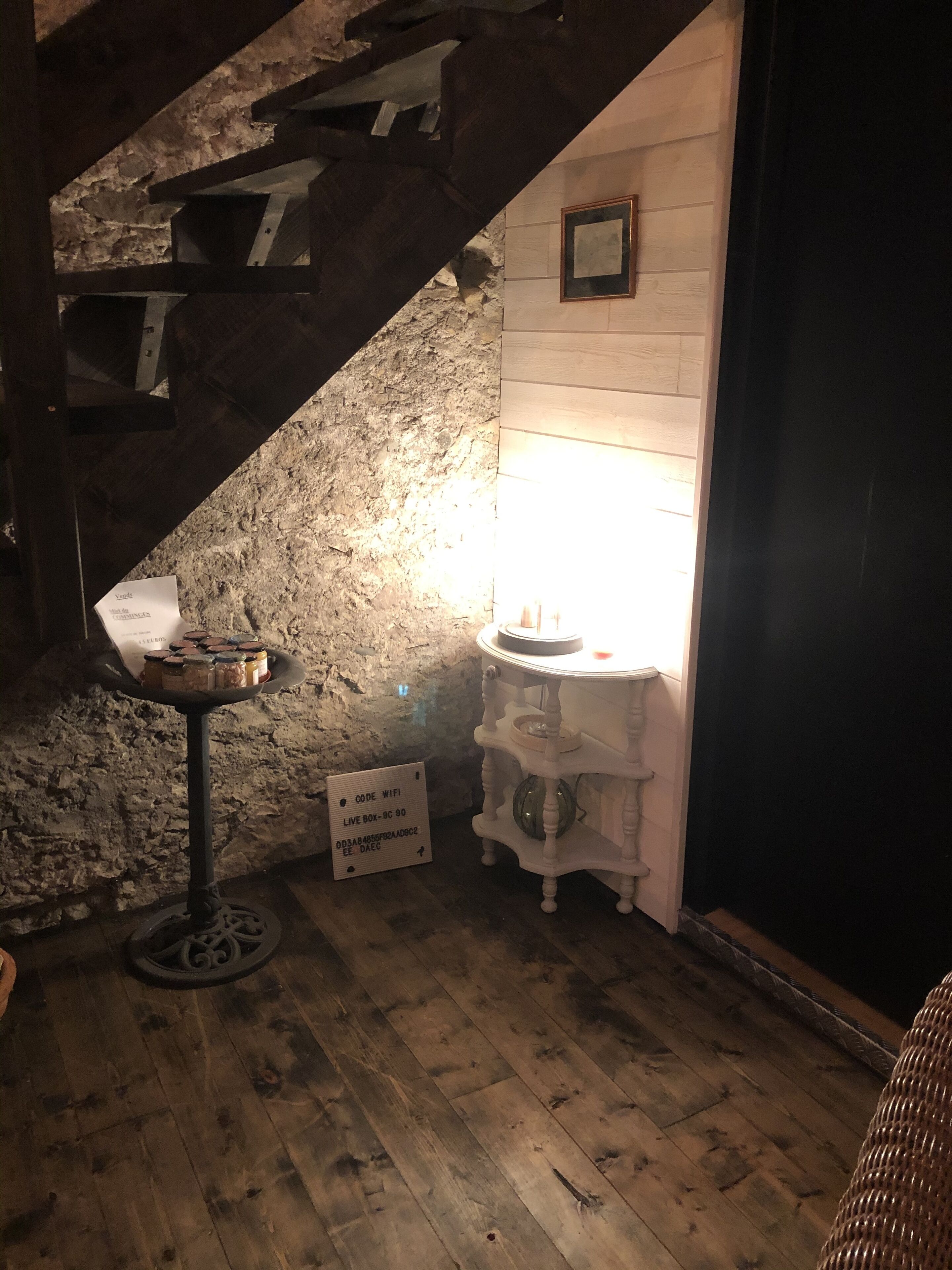 Ein rustikaler Raum mit Steinwand, Holzboden und einer Treppe. Ein Tisch mit Gläsern und ein Schild mit dem Wlan-Code.