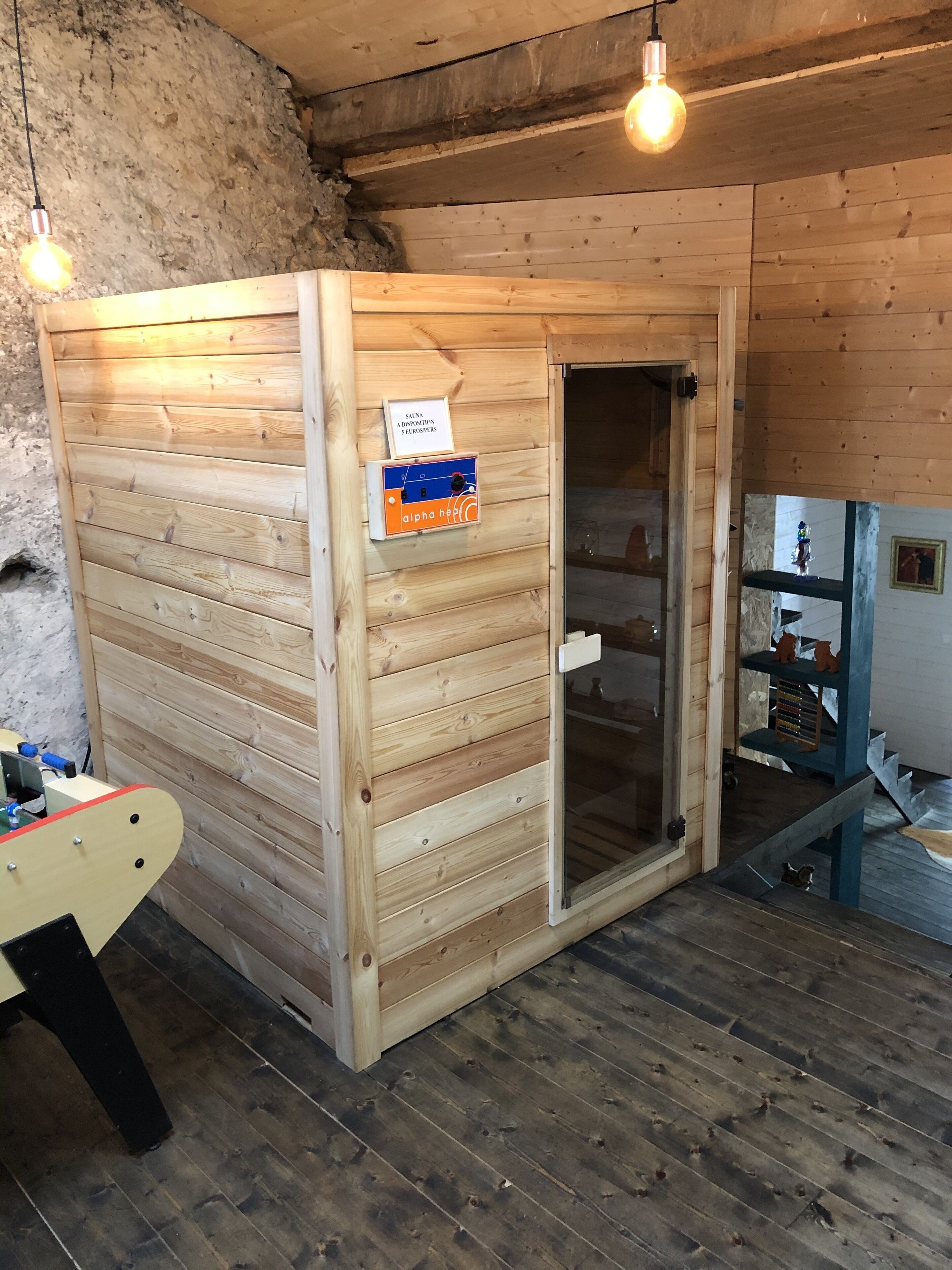 Una sala de sauna con paredes de madera y una puerta de vidrio, un panel de control y un estante pequeño con figuritas.