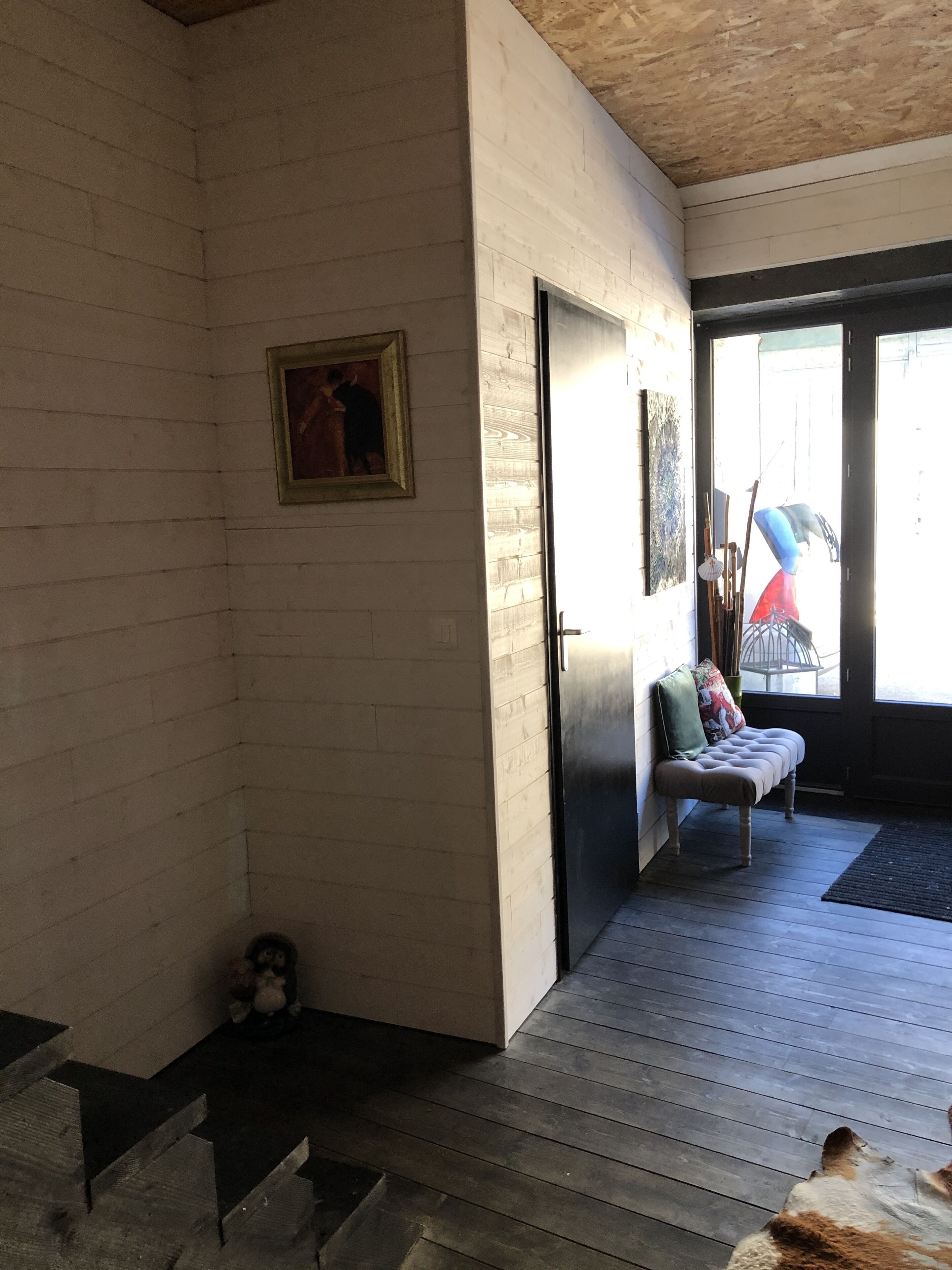 Una habitación con piso de madera, un banco, una puerta y una ventana.