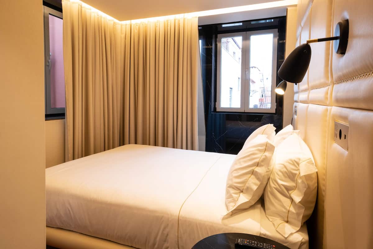 Ein Hotelzimmer mit Bett, Fenster mit Vorhängen, Nachttisch und einer Wandlampe.
