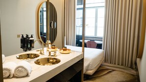A hotel bathroom with a large mirror, two sinks, and a bed.
