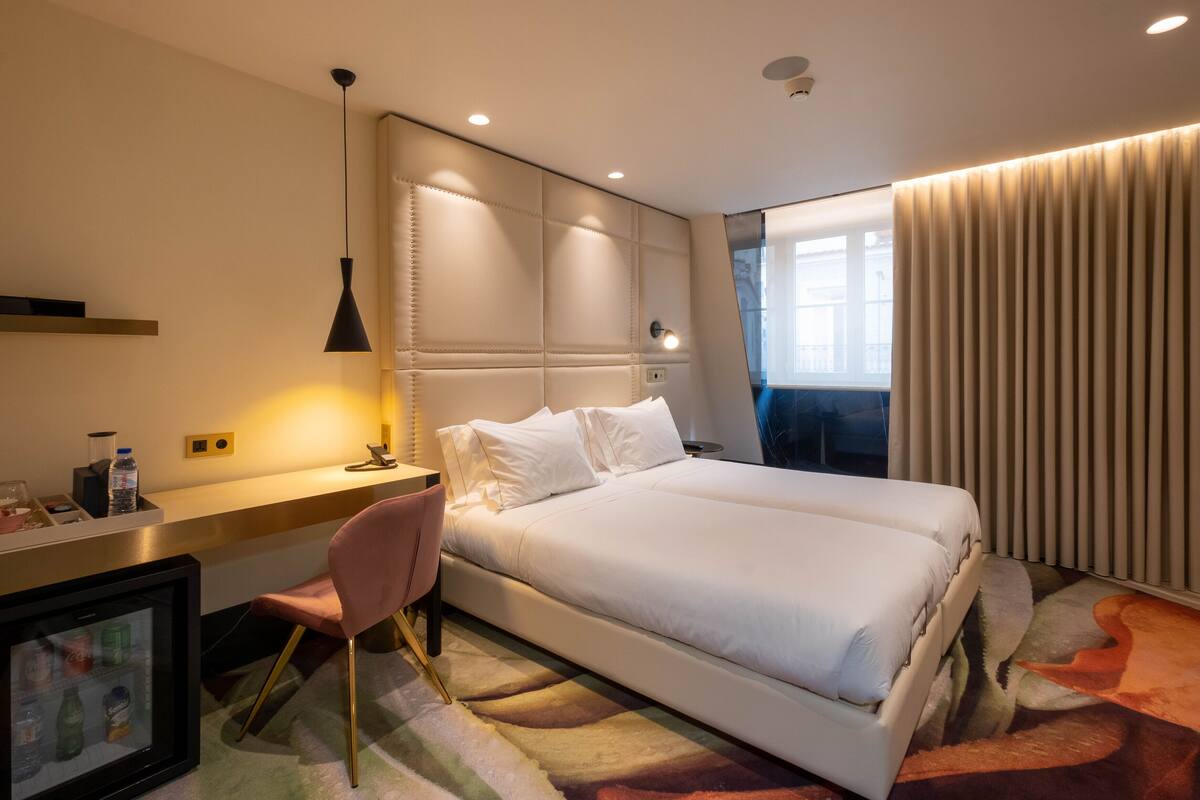 Ein Hotelzimmer mit einem großen Bett, einem Schreibtisch mit Stuhl, einem gerahmten Bild und einem Fenster mit Vorhängen.