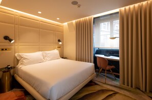 A hotel room with a large bed, a desk, and a chair. There is a window with curtains, a nightstand, and a lamp. - Madalena by The Beautique Hotels (Lisbon)