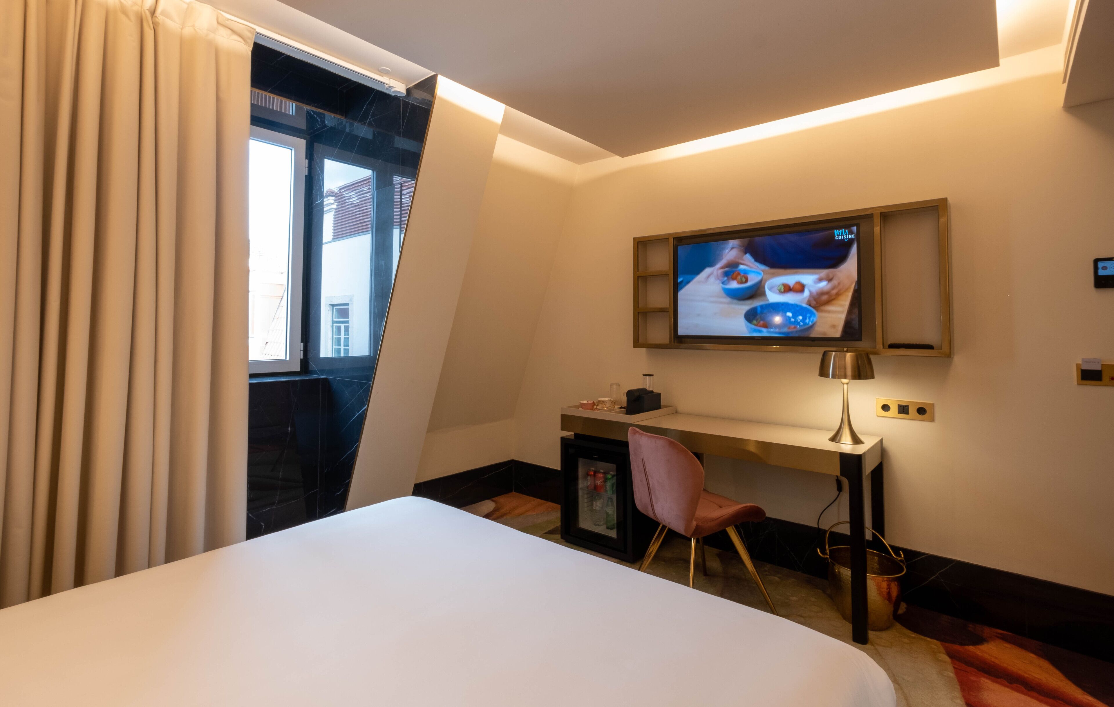 Une chambre d’hôtel avec un lit, un bureau, une télévision et une fenêtre avec des rideaux.