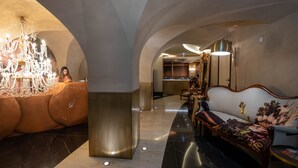 A luxurious lobby with a grand chandelier, plush seating, and a modern kitchen in the background.