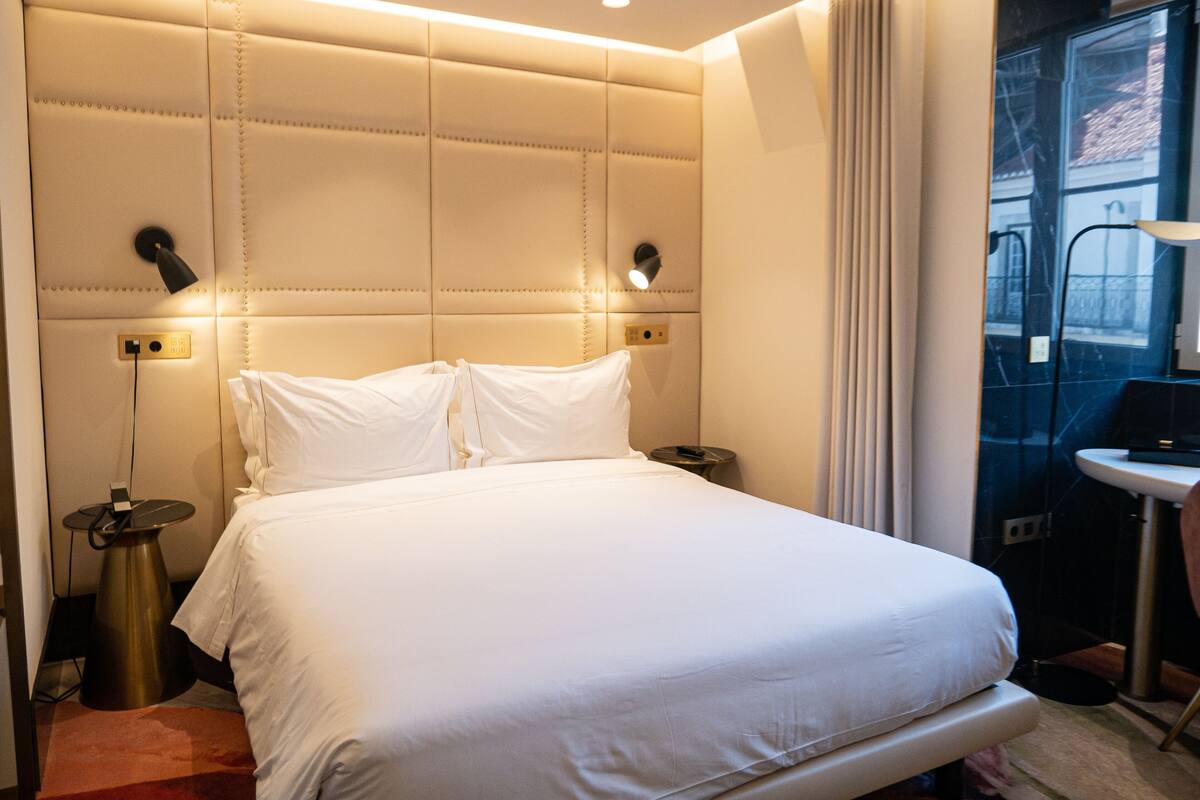 Ein Hotelzimmer mit einem großen Bett, einem Nachttisch, einer Lampe und einem Fenster mit Vorhängen.