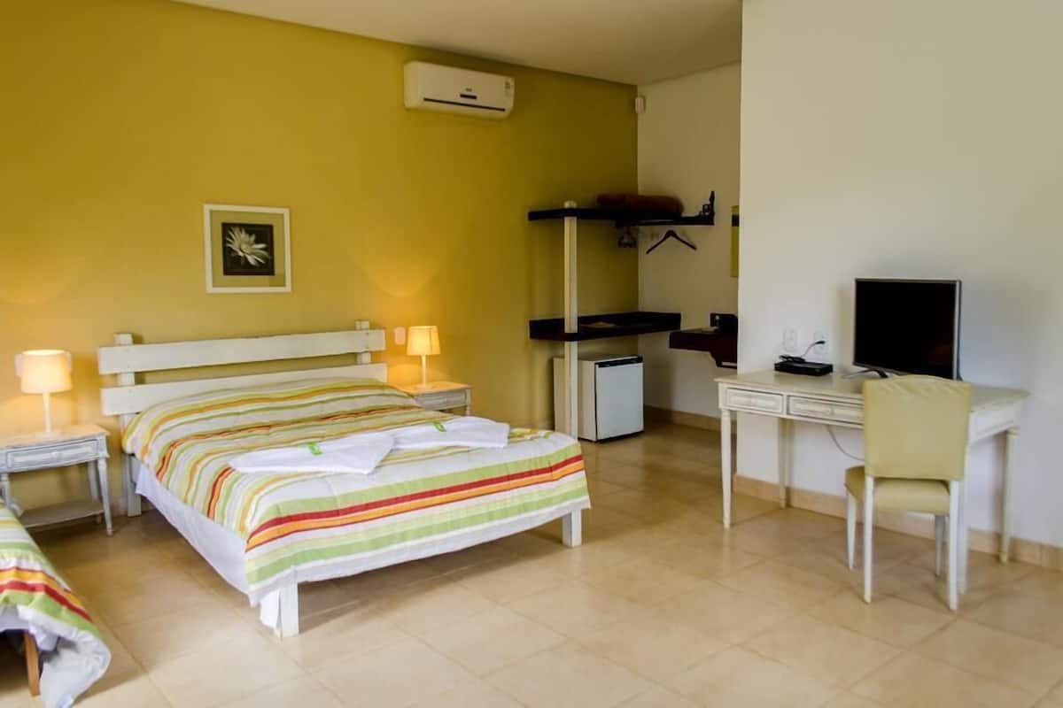 A hotel room with a bed, bedside tables with lamps, a desk with a chair, a TV, and a small refrigerator.