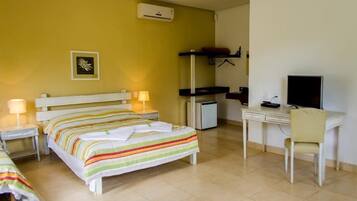 Quarto de hotel com cama, mesas de cabeceira com luminárias, escrivaninha com cadeira, televisão e um pequeno frigorífico.