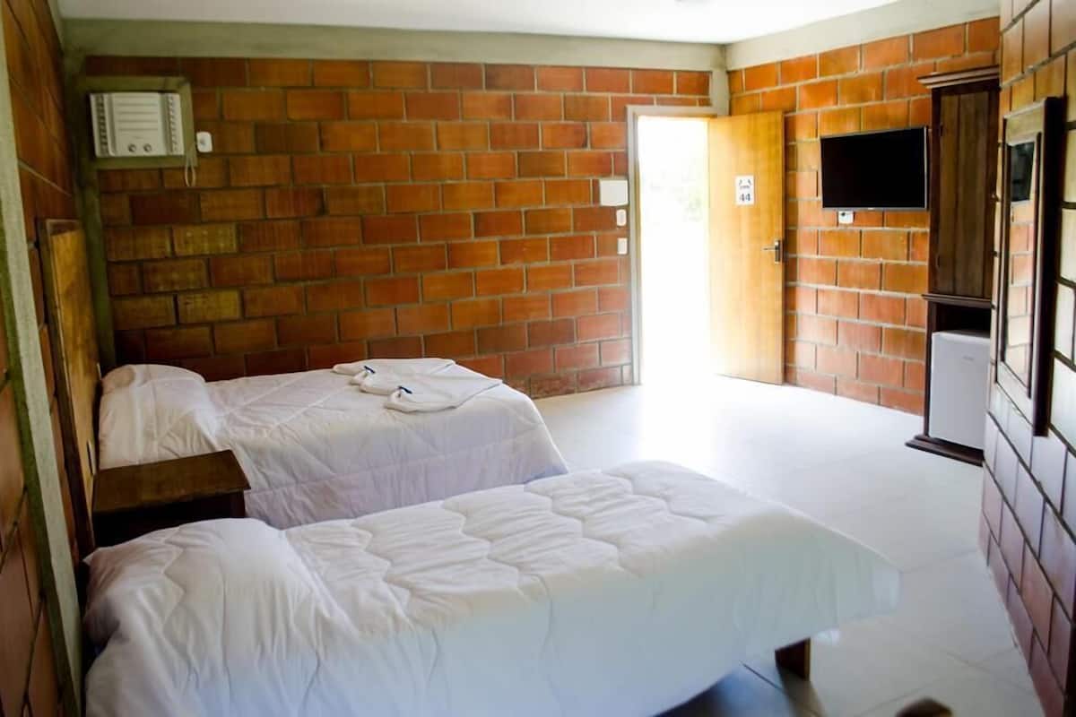 A room with two beds, a brick wall, a door, and a television mounted on the wall.