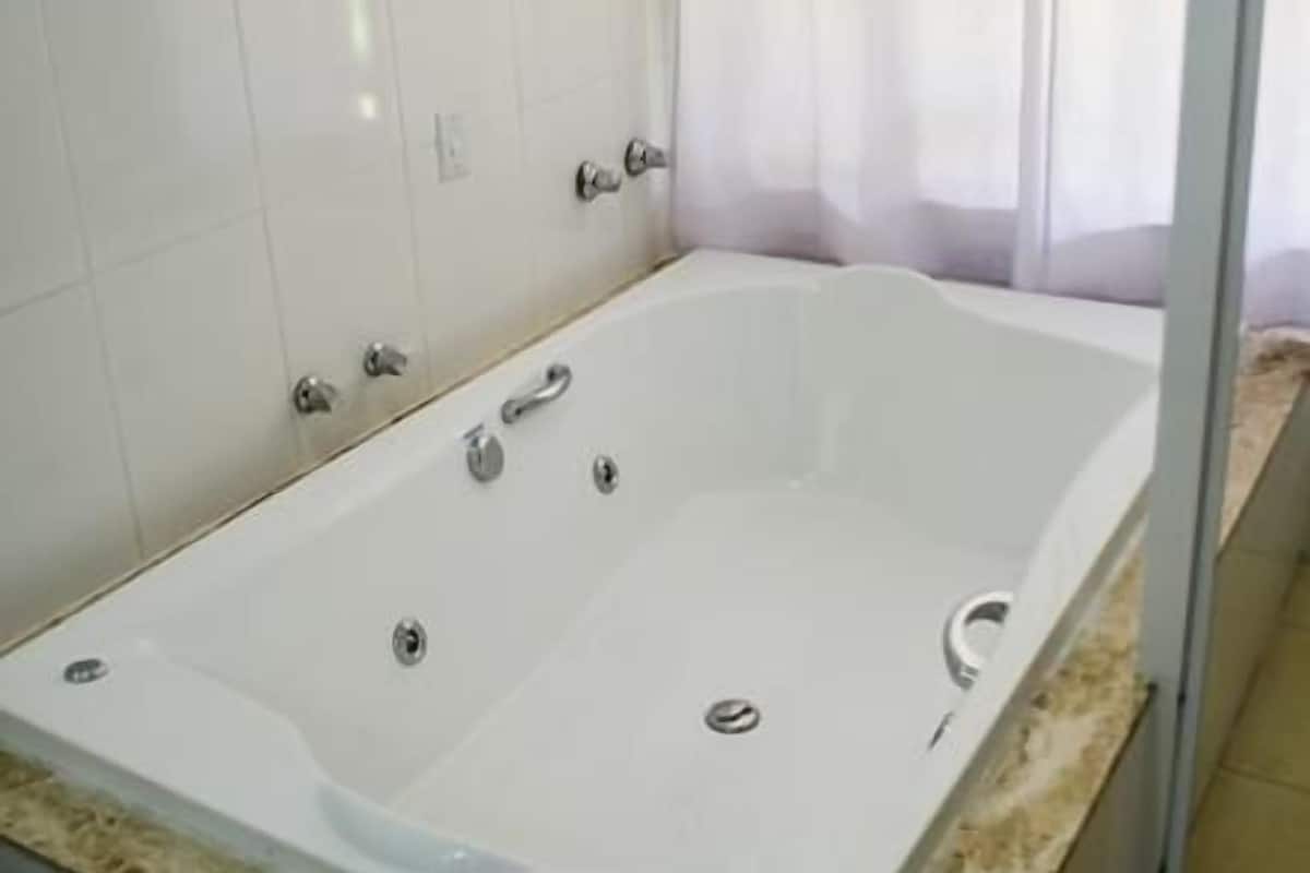 A large, rectangular bathtub with a marble countertop, a glass shower enclosure, and a white tiled wall.