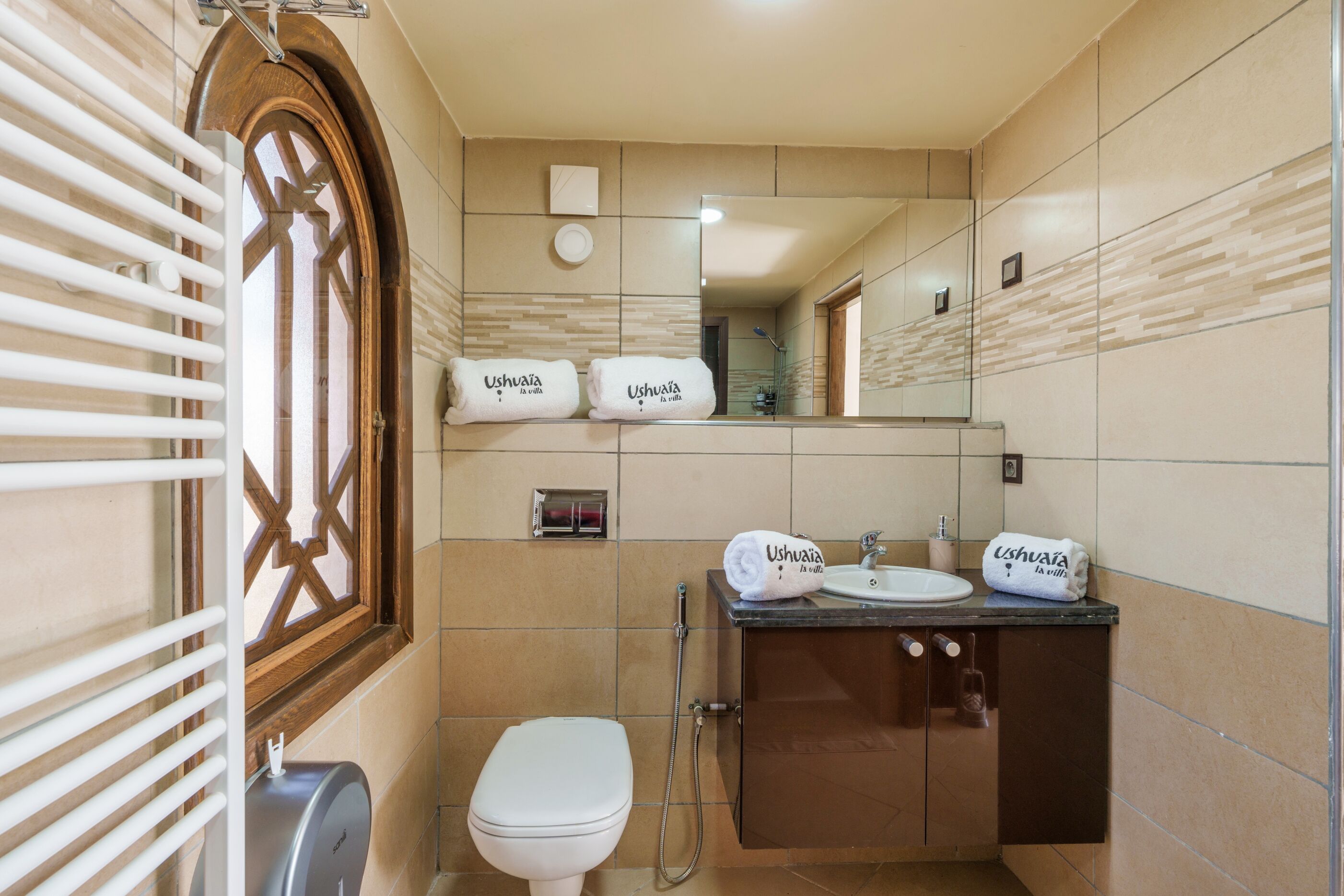 Un baño con inodoro, lavamanos y ducha. Hay toallas con el nombre "Ushuaia".