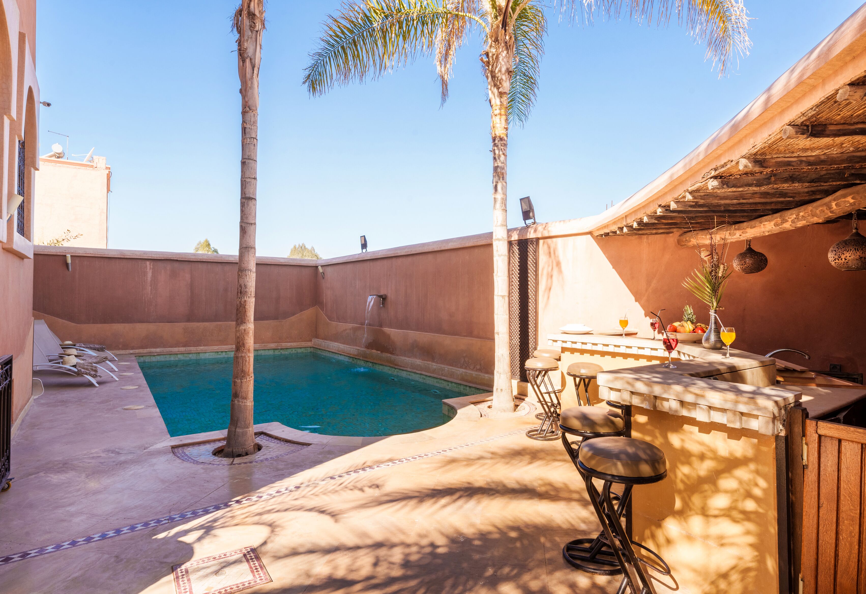 Zona de piscina con bar y asientos, rodeada de palmeras y cielo despejado.
