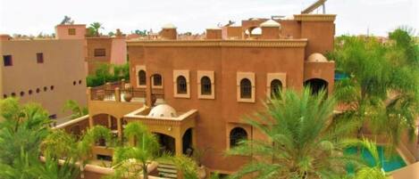 A traditional building with multiple balconies and arched windows, surrounded by palm trees and a swimming pool.